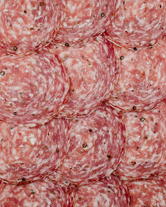 Close-up of sliced salami with a pinkish-red color and white fat streaks.