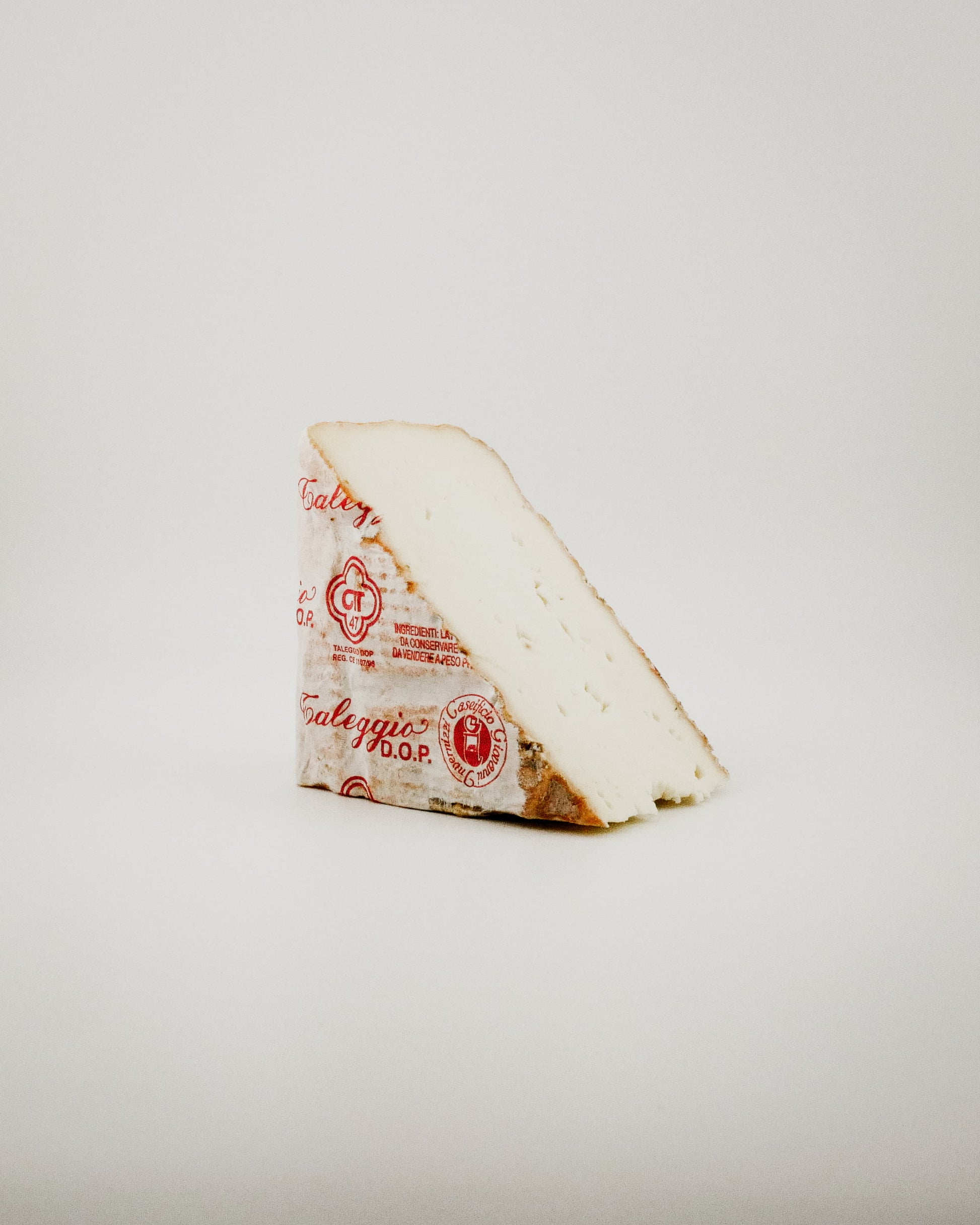 Triangular wedge of cheese an artisanal Washed-Rind Cow’s-Milk Cheese a red label on a light gray background