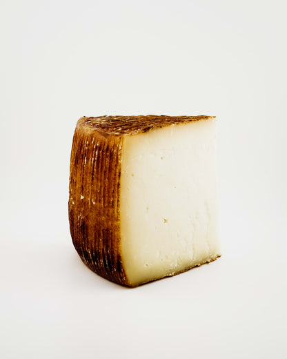 Triangular piece of cheese with a brown rind on a white background